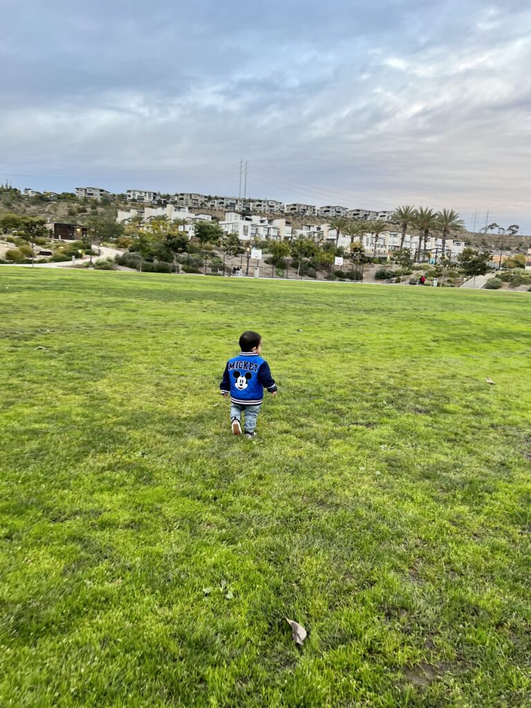 toddler running outdoors in grass field 